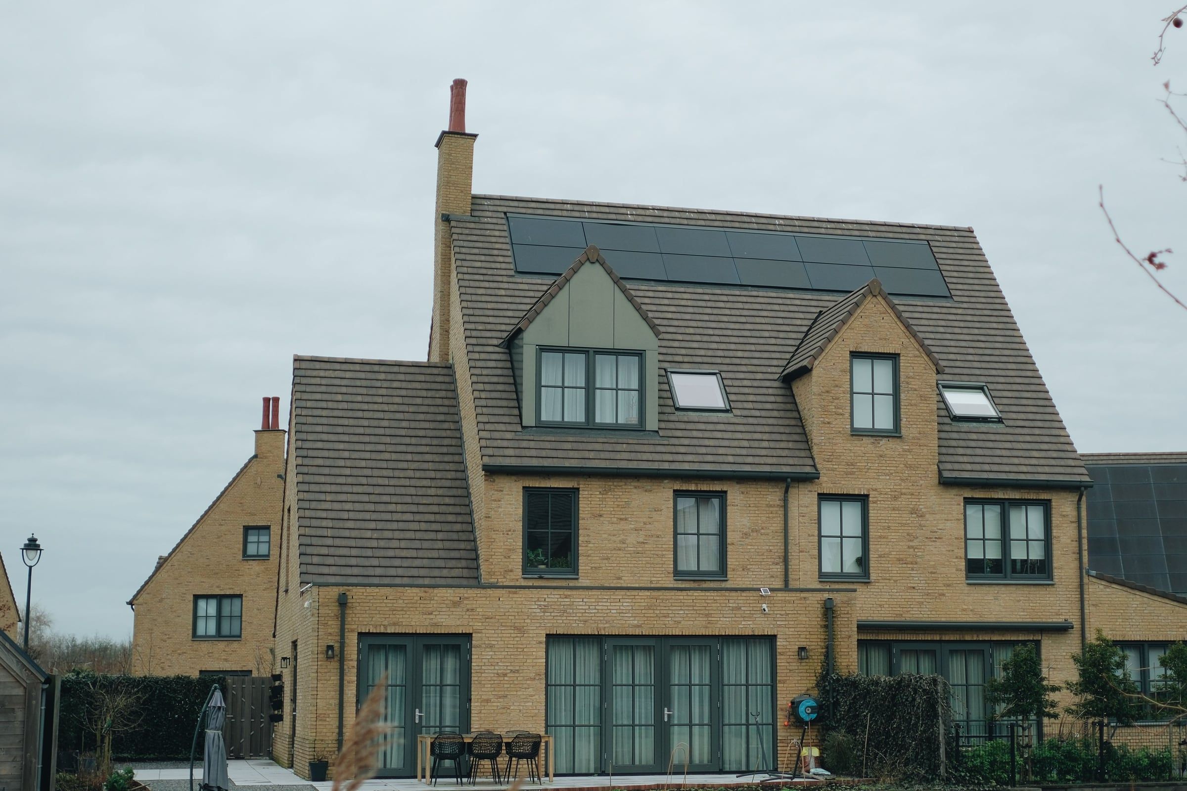 A brick house with dormer windows and a bank of solar panels across the upper roof slope.